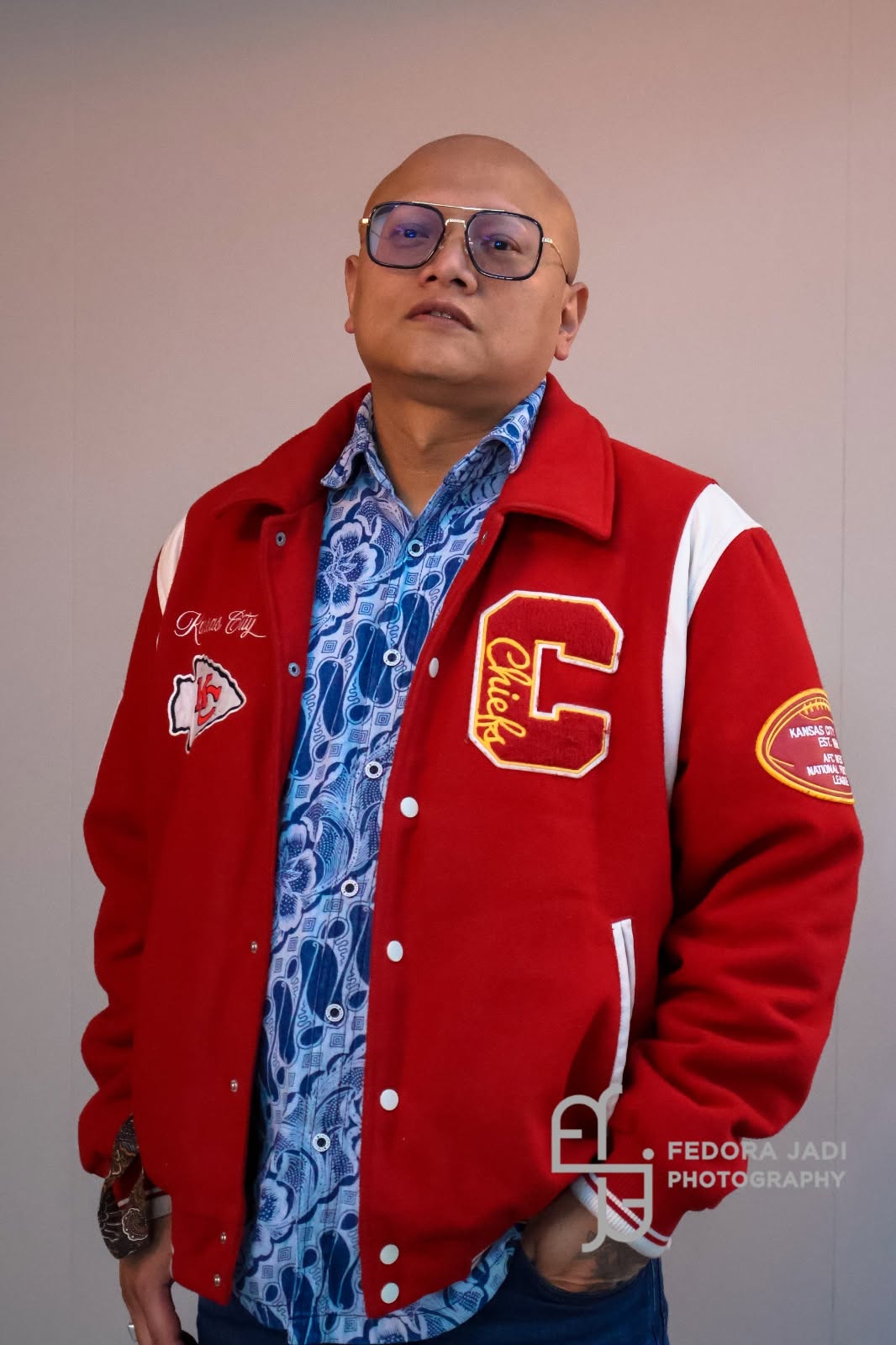 Virgil Wongsokario in een rood varsityjack over een blauw batikoverhemd