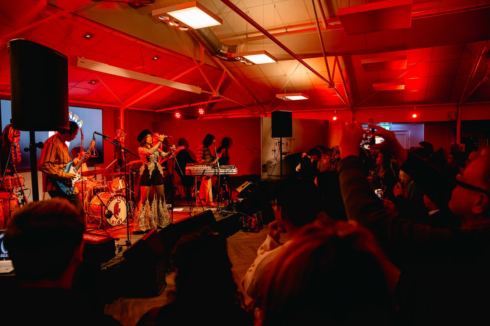 Band op het podium in rood licht, publiek filmt mee